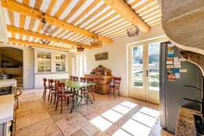 Una cocina con techo de madera, una mesa de comedor con sillas, un refrigerador y una ventana con vista a follaje.