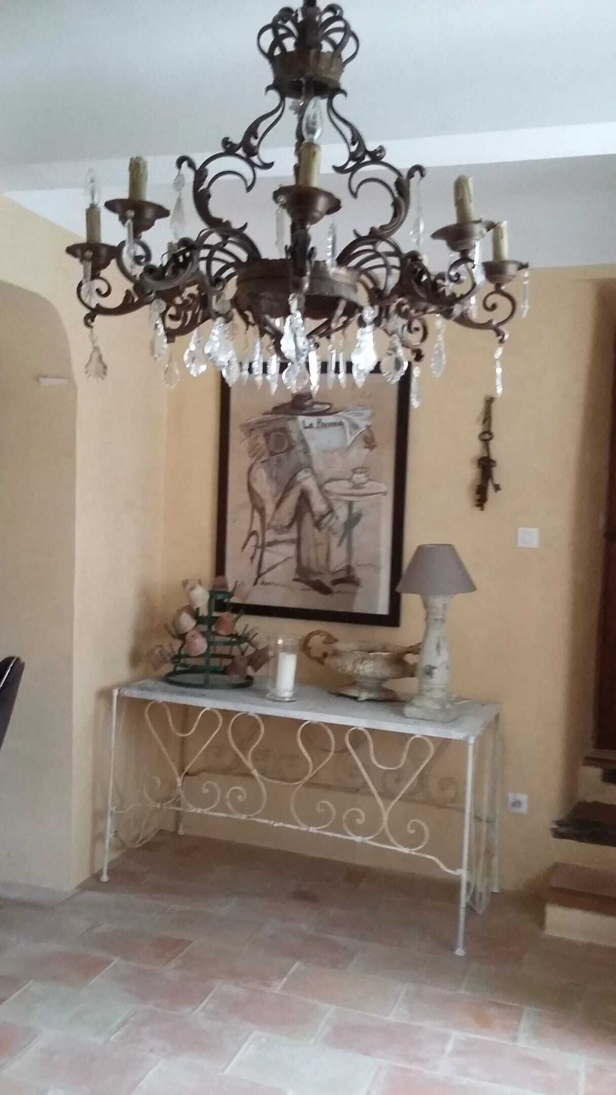 Ein Zimmer mit einer verzierten Schmiedeeisen-Konsole, einem gerahmten Kunstwerk, einer Chandelüster und einer Lampe.