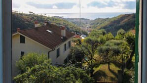 Ein Gebäude mit geneigtem Dach, umgeben von üppiger Vegetation und Blick auf eine entfernte Küstenlinie.