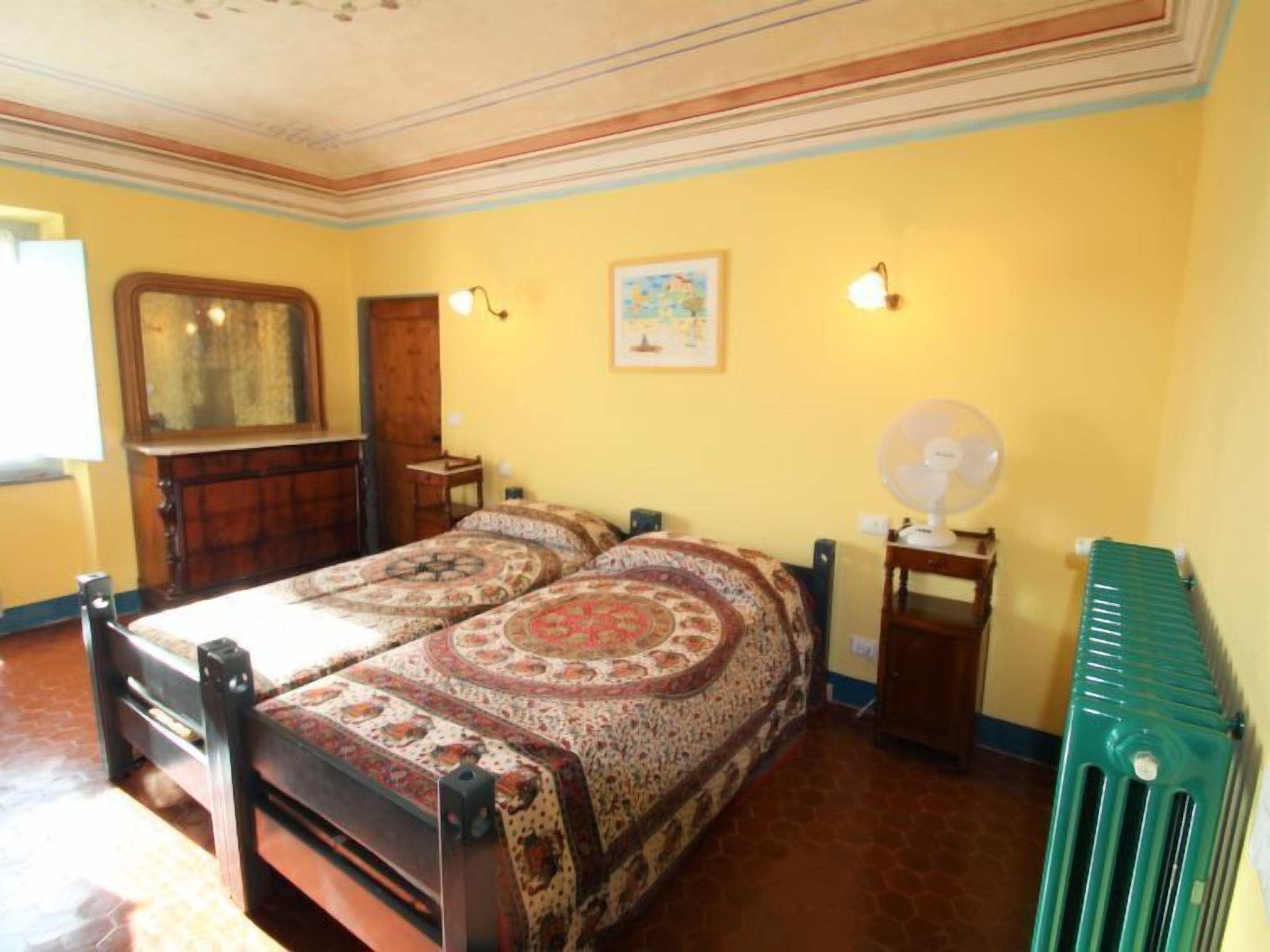 Une chambre avec un grand lit, une armoire en bois, une petite table, une lampe fixée au mur et un radiateur.