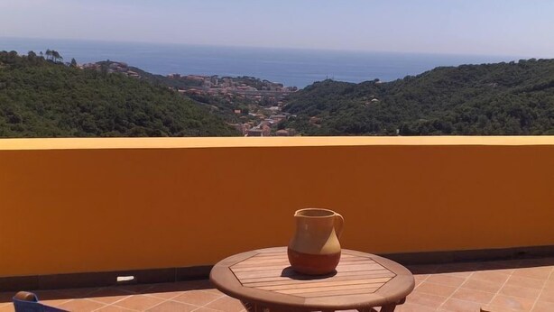 Ein Balkon mit Blick auf eine Küstenstadt, ein Tisch mit einer Vase und eine gelbe Wand.