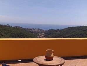 Ein Balkon mit Blick auf eine Küstenstadt, ein Tisch mit einer Vase und eine gelbe Wand.