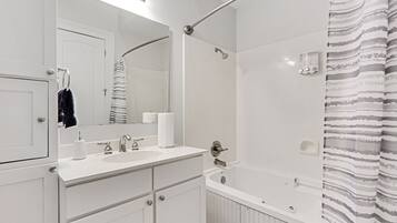 Une salle de bain moderne avec un meuble-lavabo blanc, un grand miroir, une douche et un rideau de douche à rayures.