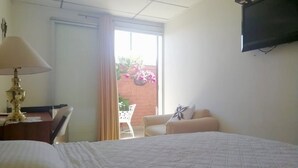 Habitación de hotel con cama, escritorio con lámpara, televisor montado en la pared y balcón con plantas.