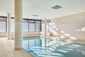 An indoor swimming pool with tiled walls and ceiling, clear glass panels, and a tiled floor.