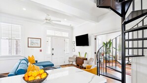 A spacious living room with a white marble coffee table, a blue sofa, and a black spiral staircase. - 8C at Saint Philip Square, One Block to King, Bright Enchanting Top Floor Apt (Charleston)