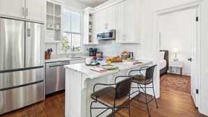 A modern kitchen with white cabinetry, stainless steel appliances, and a central island with bar stools. - 8C at Saint Philip Square, One Block to King, Bright Enchanting Top Floor Apt (Charleston)