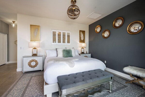 Un dormitorio con una cama grande, lámparas de noche, un espejo decorativo e iluminación empotrada en la pared.