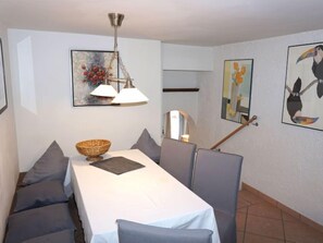 A dining area with a table set for four, grey upholstered chairs, a hanging light fixture, and framed artwork on the walls.