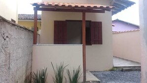 Ein kleines Haus mit Ziegeldach, einer Holzterrasse und einem Fenster mit roten Fensterläden.