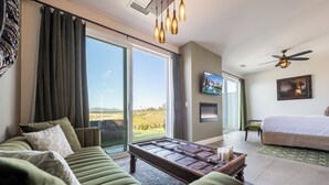 Habitación de hotel moderna con un sofá verde, una mesa de centro de madera, una cama y un ventanal con vistas al exterior.