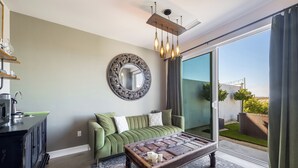 Una sala de estar moderna con un sofá verde, una mesa de centro, un espejo grande y un puerta corrediza de vidrio que da a un balcón.