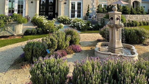 Una casa señorial con una llamativa puerta principal negra, fachada de piedra y un jardín cuidado con una fuente.