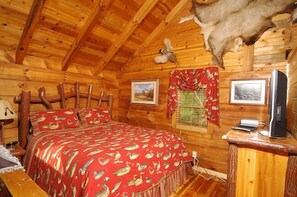 A log cabin room with a bed, wooden walls, a mounted animal head, and two framed pictures.