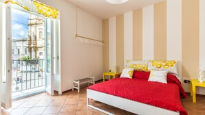 A bedroom with a white bed, red bedding, and a view of a cityscape through a large window. - Edy Apartment (Palermo)