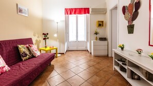 A living room with a red sofa, a small yellow table with a vase of flowers, a white cabinet, and a wall-mounted cactus decoration. - Edy Apartment (Palermo)