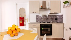 A kitchen with a stove, oven, and sink. There is a table with a bowl of oranges. - Edy Apartment (Palermo)