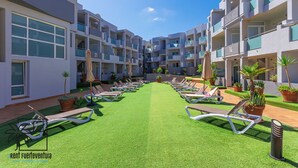 A courtyard with multiple lounge chairs and potted plants, surrounded by modern buildings with balconies.