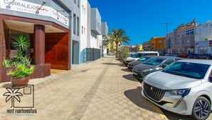 A modern building with a sign for 'CORRALEJO Apartments' and a parking area with several cars.
