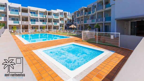 A resort with two swimming pools, a tiled deck, and a building with balconies.