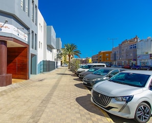 Um edifício moderno com uma placa indicando 'CORRALEJO Apartments' e uma área de estacionamento com vários carros.