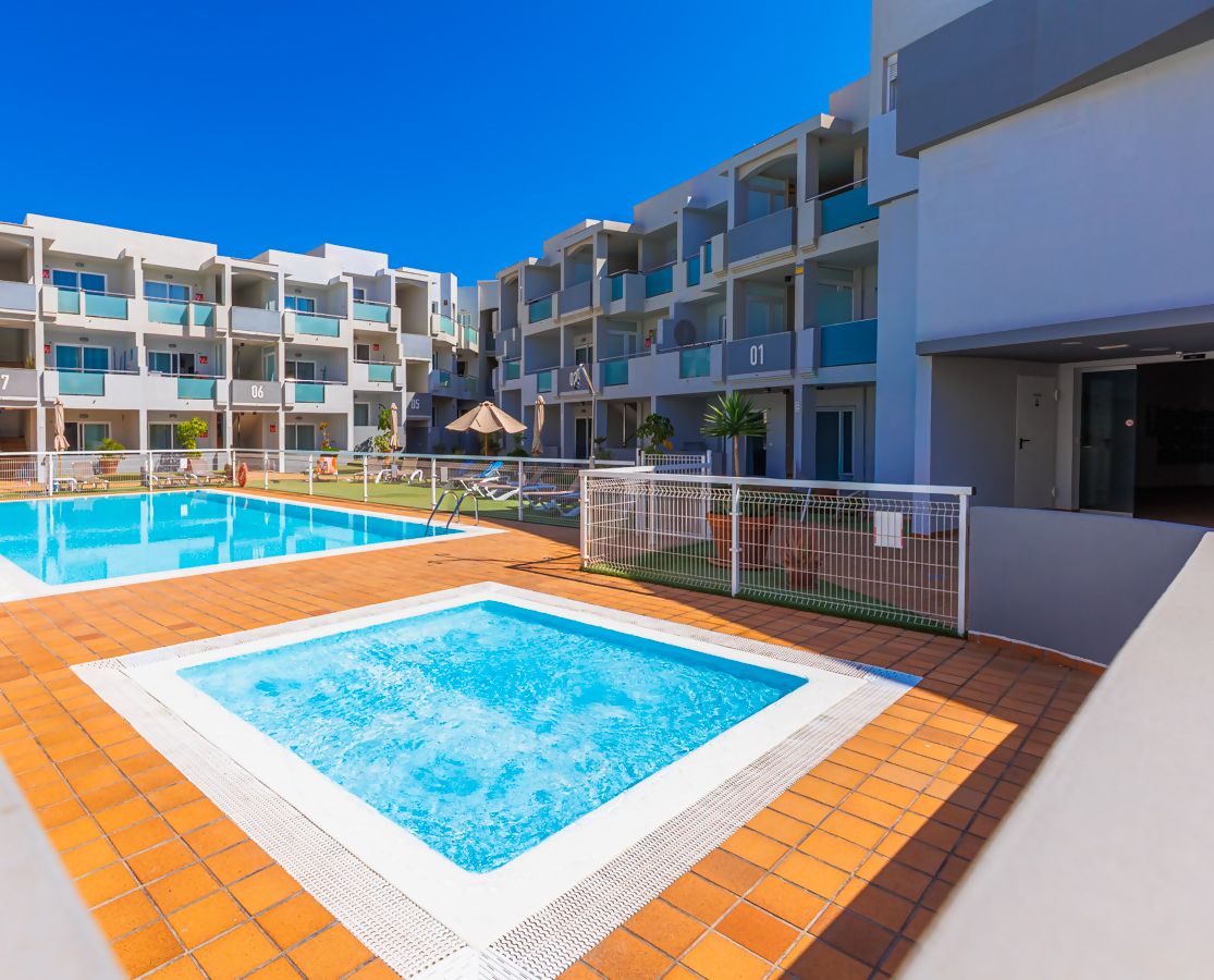 Ein Resort mit zwei Schwimmbecken, einer gefliesten Terrasse und einem Gebäude mit Balkonen.