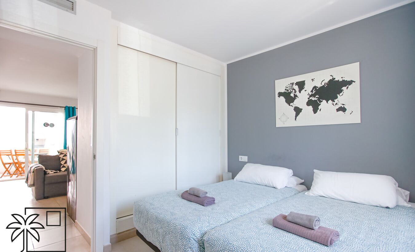 Habitación de hotel con dos camas, un mapa mundial en la pared y vistas al balcón exterior.