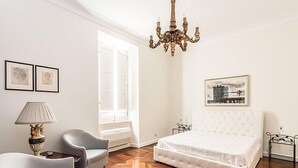A bedroom with a large bed, a chandelier, a window with a view, and two armchairs. - Apartment Silla by Interhome (Roma: Vaticano)