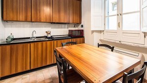 A kitchen with wooden cabinets, a black countertop, a red microwave, and a dining table with chairs. - Apartment Silla by Interhome (Roma: Vaticano)