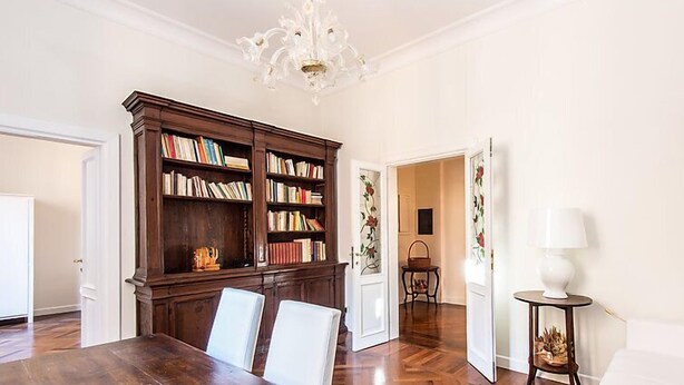 A dining room with a wooden table and chairs, a large bookcase, and a chandelier. - Apartment Silla by Interhome (Roma: Vaticano)