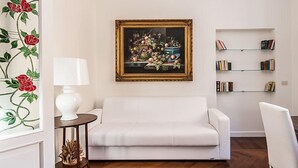 A living room with a white sofa, a painting of fruit, a lamp, and a bookshelf. - Apartment Silla by Interhome (Roma: Vaticano)