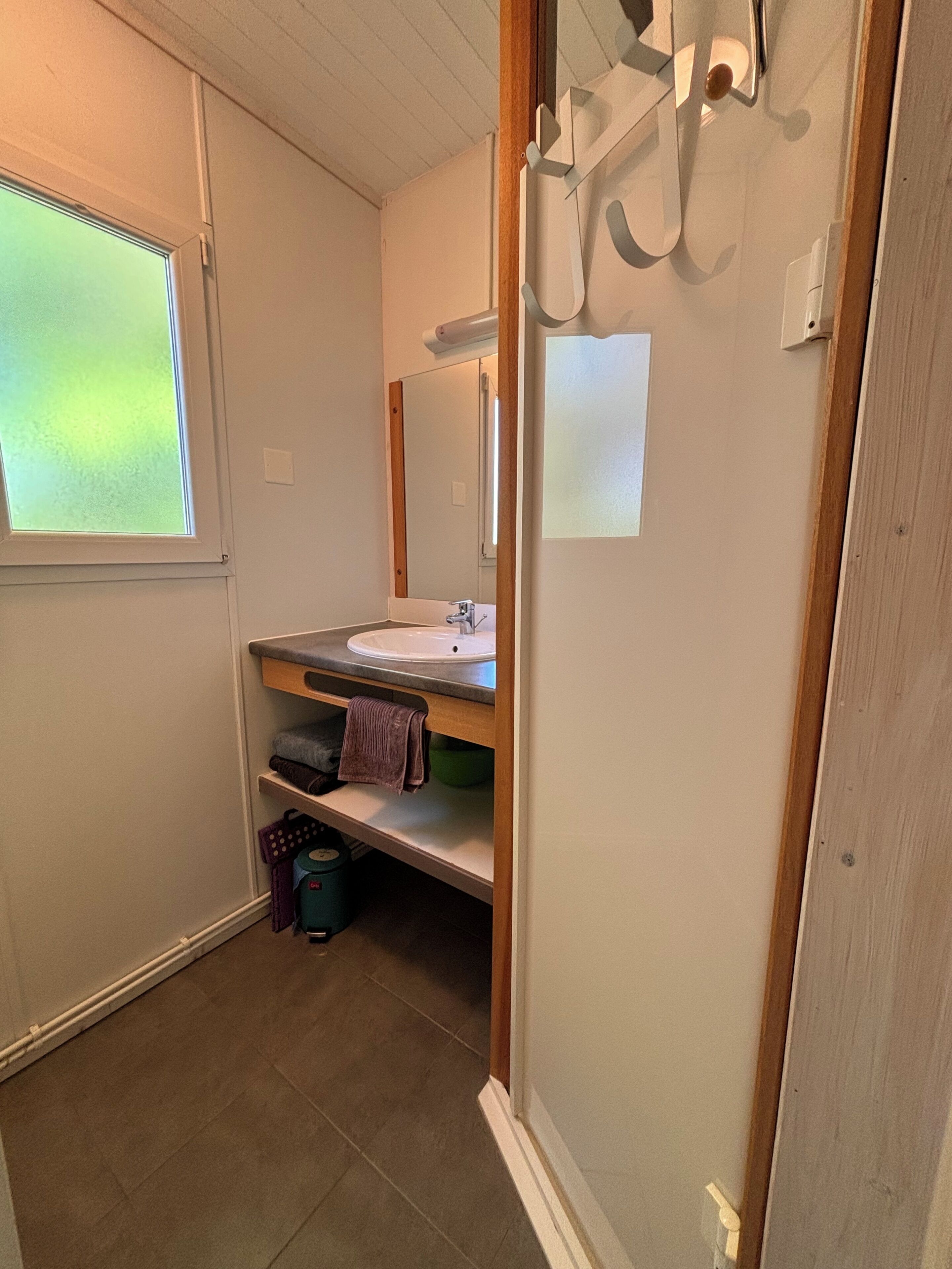 Une salle de bain avec un lavabo, un miroir, un porte-serviettes et une fenêtre.
