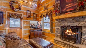 A cozy log cabin interior with a fireplace, wooden walls, a television, and a comfortable seating area.