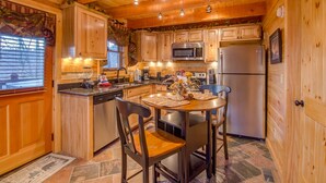 A wooden cabin kitchen with a central island, stainless steel appliances, and a dining area with two chairs.