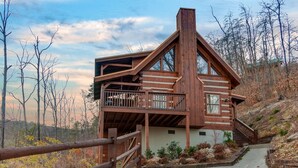 A cabin with a wooden exterior, a balcony, and a staircase leading to the upper level.