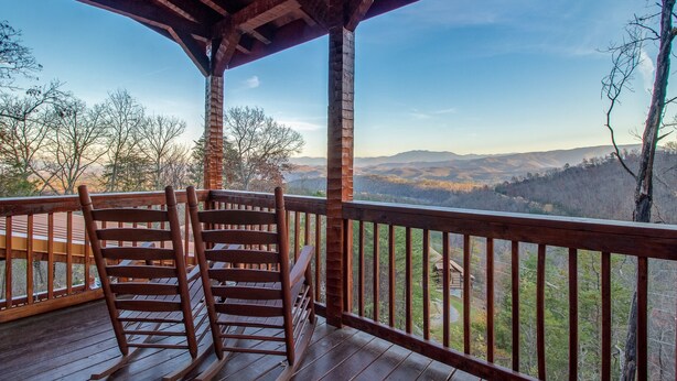 A wooden deck with a rocking chair and a view of a mountainous landscape.