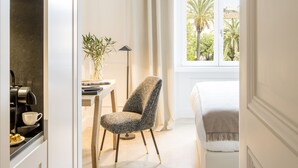 A modern hotel room with a bed, a chair, a small table with a plant, and a window with a view of palm trees. - Residenza B (Rome)