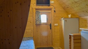 A cozy wooden cabin room with a bed, a small desk, a television, and a door with a window.