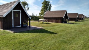 A row of rustic wooden cabins with pitched roofs, a picnic table, and a well-maintained lawn.