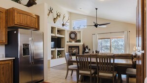 Une cuisine équipée d’un réfrigérateur en acier inoxydable, de meubles en bois, d’une table à manger avec des chaises, d’une cheminée et de têtes d’animaux fixées au mur.