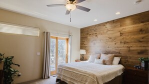 Une chambre à coucher avec un grand lit, un ventilateur de plafond, une tête de lit en bois, une table de chevet et une plante en pot.