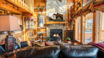 A cozy log cabin interior with a fireplace, leather sofa, wooden walls, and various decorations.