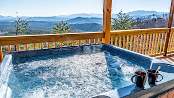 A hot tub with two mugs on a wooden deck overlooking a mountainous landscape.