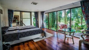 Une chambre avec un grand lit, une table en verre et une vue sur les palmiers, visible à travers de grandes fenêtres.