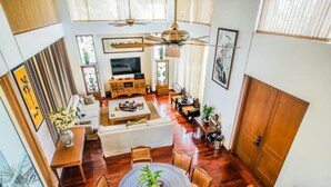 Un vaste espace de vie doté d’un haut plafond, d’un plancher en bois, d’un coin salon central avec un canapé et une table basse, d’un téléviseur et d’un ventilateur de plafond.