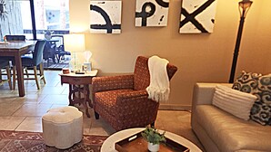 A living room with a patterned armchair, a round coffee table with a tray, a sofa with patterned cushions, and abstract wall art. - South Palm Springs 2BR Condo. Affordable. Pool, Hot Tub, Golf, Hiking,
Tennis! (Palm Springs)