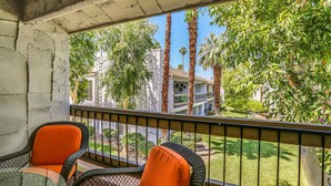A balcony with wicker chairs and a table, overlooking a well-maintained garden and residential buildings. - South Palm Springs 2BR Condo. Affordable. Pool, Hot Tub, Golf, Hiking,
Tennis! (Palm Springs)