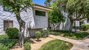 A modern building with a stone facade, numbered windows, and a well-maintained garden with trees and shrubs. - South Palm Springs 2BR Condo. Affordable. Pool, Hot Tub, Golf, Hiking,
Tennis! (Palm Springs)