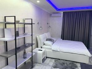 A modern bedroom with a white bed, a small white nightstand, a white shelf unit, and a grey curtain. - VIP Apartment (Kyiv)