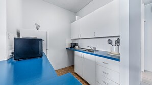 Uma cozinha compacta com armários brancos, bancada azul e painel atrás do fogão em azulejo.